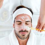 Man with clay facial mask in beauty spa.