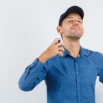 young-man-spraying-perfume-himself-blue-shirt-cap-looking-elegant-front-view